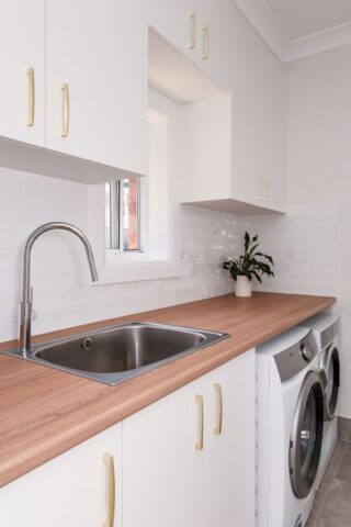 modern renovated laundry with brass handles and white cabinetry